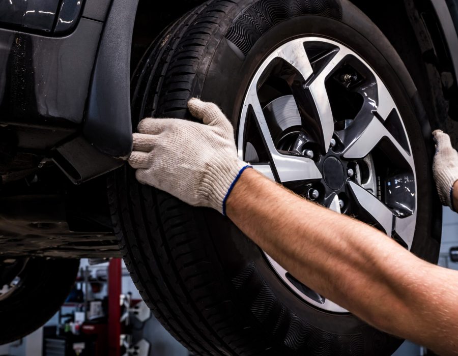 Close-up of mechanic in a car service removes a wheel from a car manually