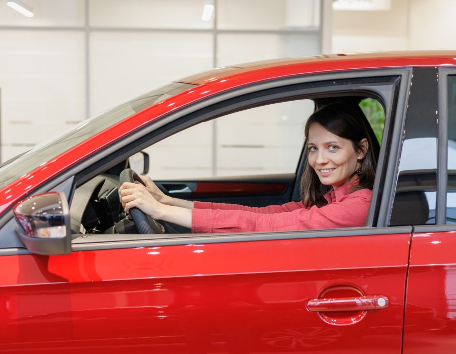 happy European woman in a red car at a car dealership, buying a car on credit or trade in.