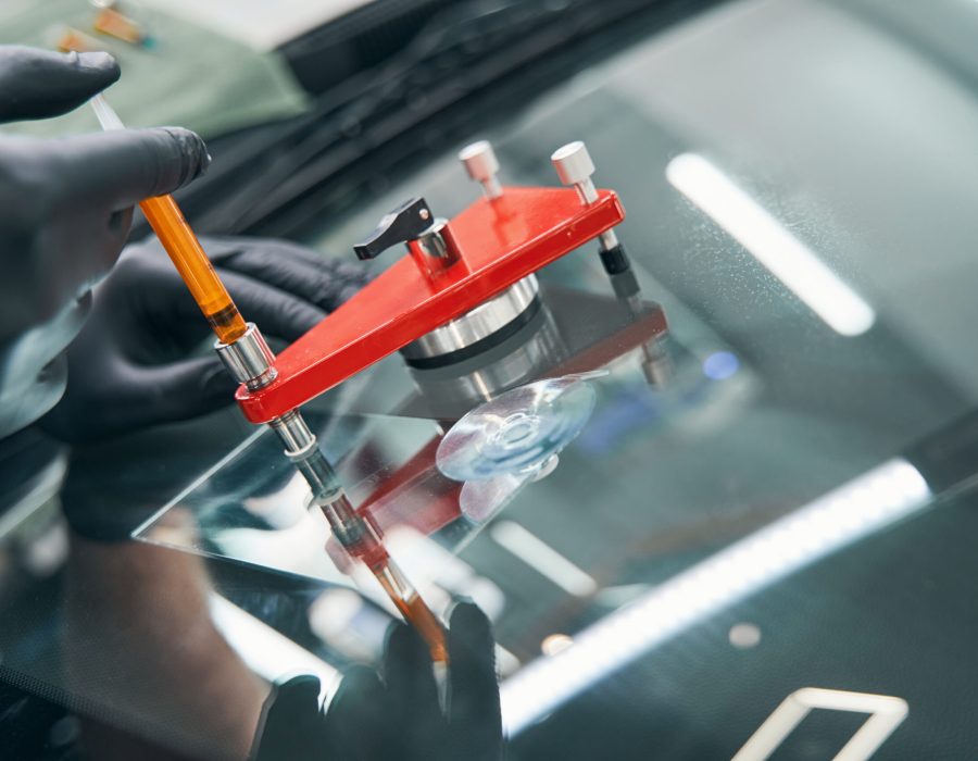Serviceman in workshop fixing broken car window with vacuum filler. Professional auto glass repair